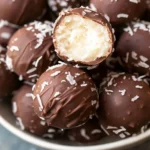 Bite-sized chocolate coconut balls with shredded coconut topping, revealing a creamy coconut filling inside.