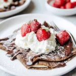 Chocolate crepes folded with whipped cream, strawberries, and drizzled with chocolate sauce