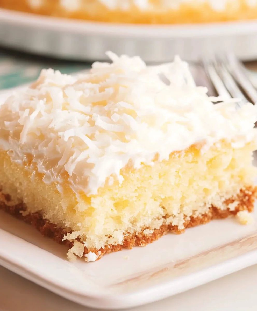 A piece of Coconut Cream Poke Cake with a golden base and creamy coconut topping.
