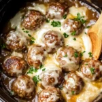 Slow-cooked French onion meatballs topped with melted Gruyere cheese and fresh herbs in a crockpot.