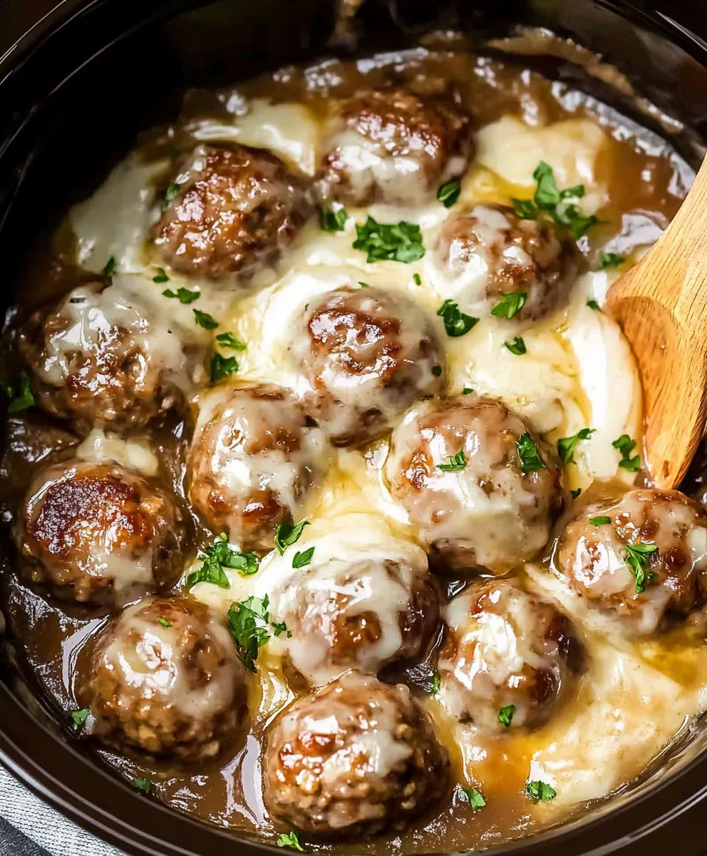 Slow-cooked French onion meatballs topped with melted Gruyere cheese and fresh herbs in a crockpot.