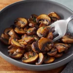 Golden brown sautéed mushrooms in garlic butter served in a dark bowl