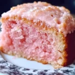 A close-up of a moist slice of strawberry cake with creamy pink frosting on a floral-patterned plate