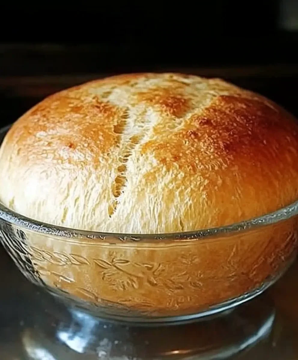 Artisan-style peasant bread rising high in a buttered bowl