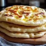 Stack of soft and puffy yogurt flatbreads with golden-brown tops, served on a wooden board.