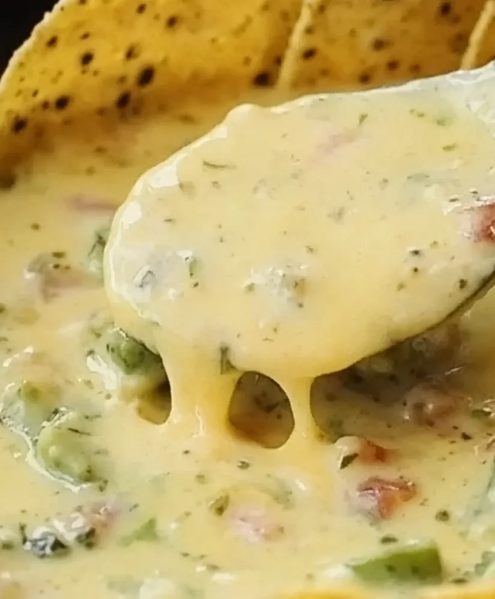 Spoon lifting a portion of The Greatest Queso That Ever Lived, highlighting the smooth and cheesy consistency.