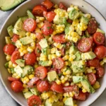 Bright corn tomato avocado salad in a bowl with sliced avocado on the side, showcasing vibrant summer produce.